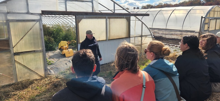 Students look on at Matt Kroul who is standing in front of a greenhouse