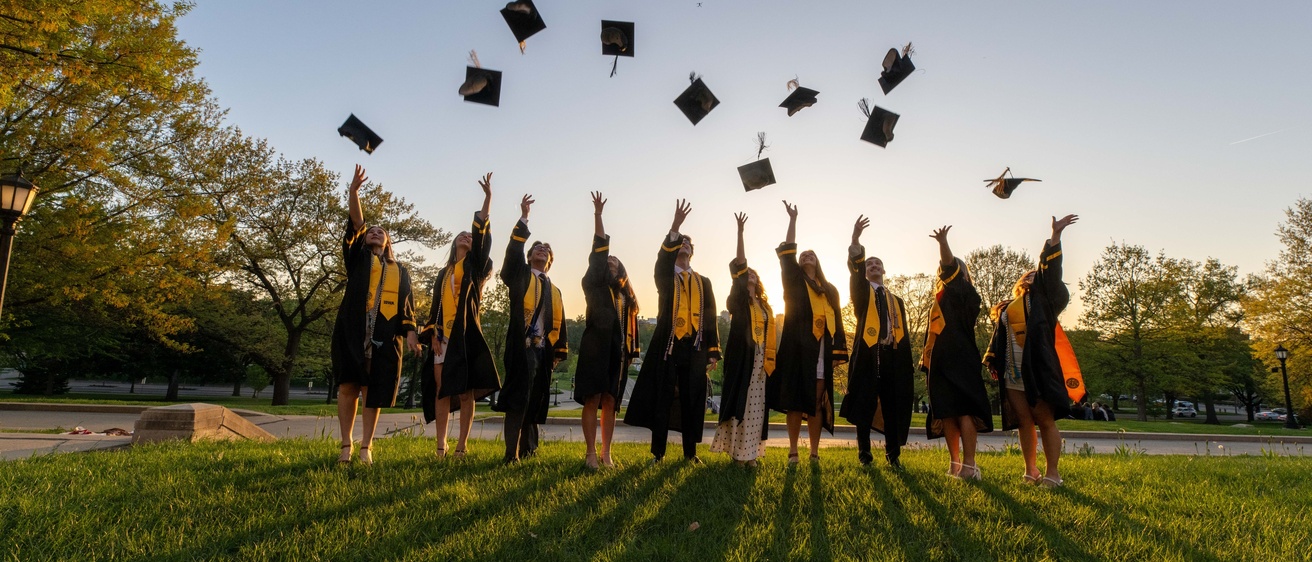 Students tossing graduation caps on Pentacrest at sunset