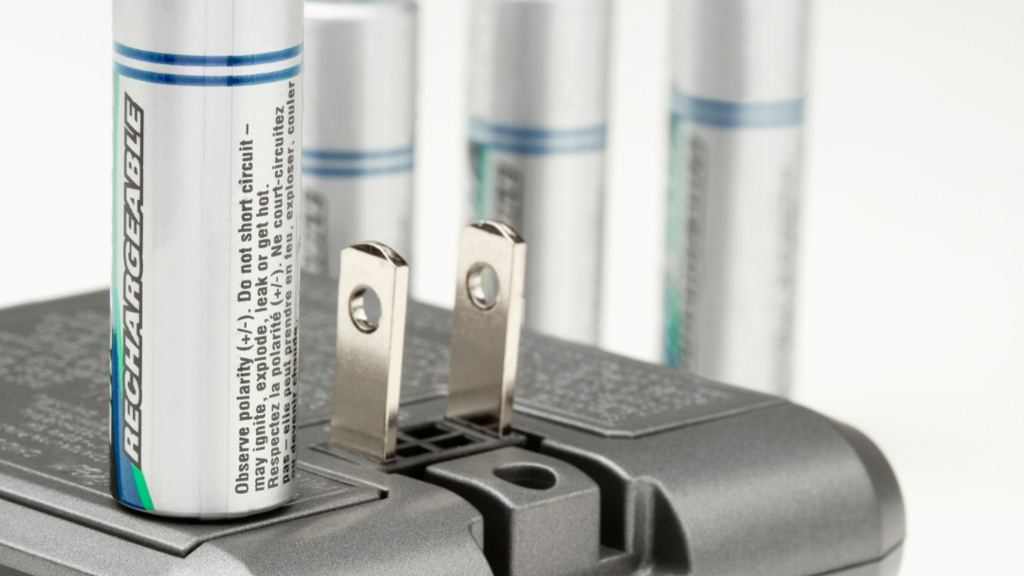 Four AA rechargeable batteries standing upright by a charger device
